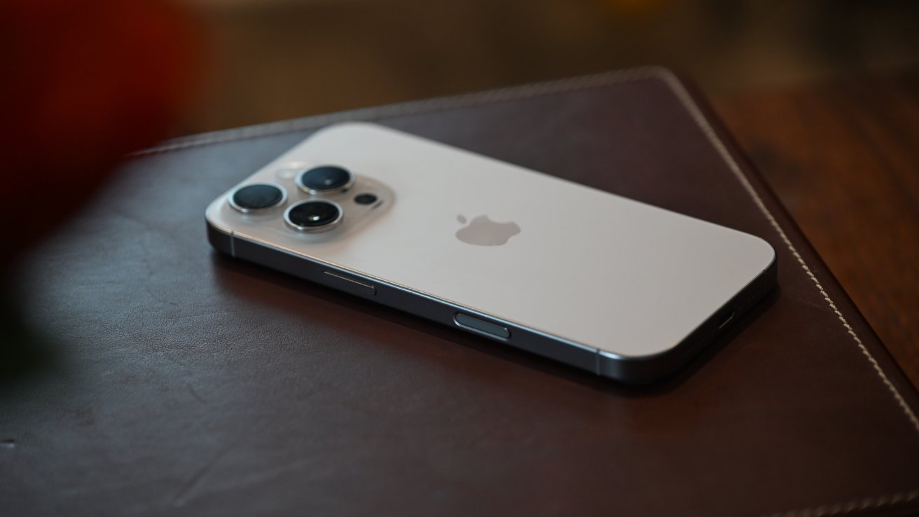 A silver smartphone with a triple-lens camera setup rests on a brown leather surface.
