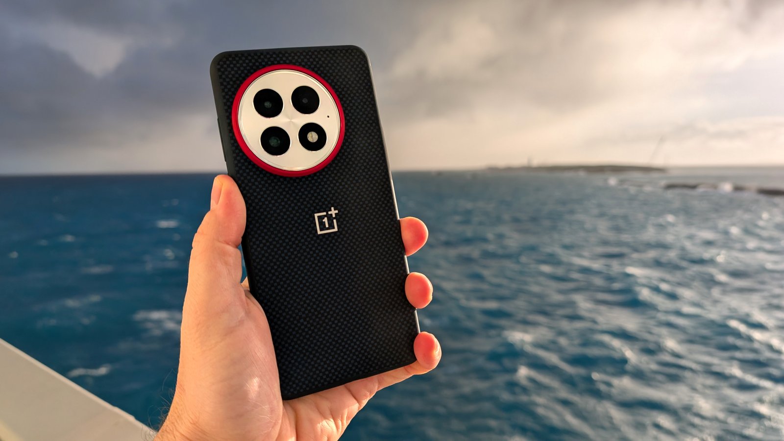 Holding the OnePlus 13 in its blue case with the ocean in the background