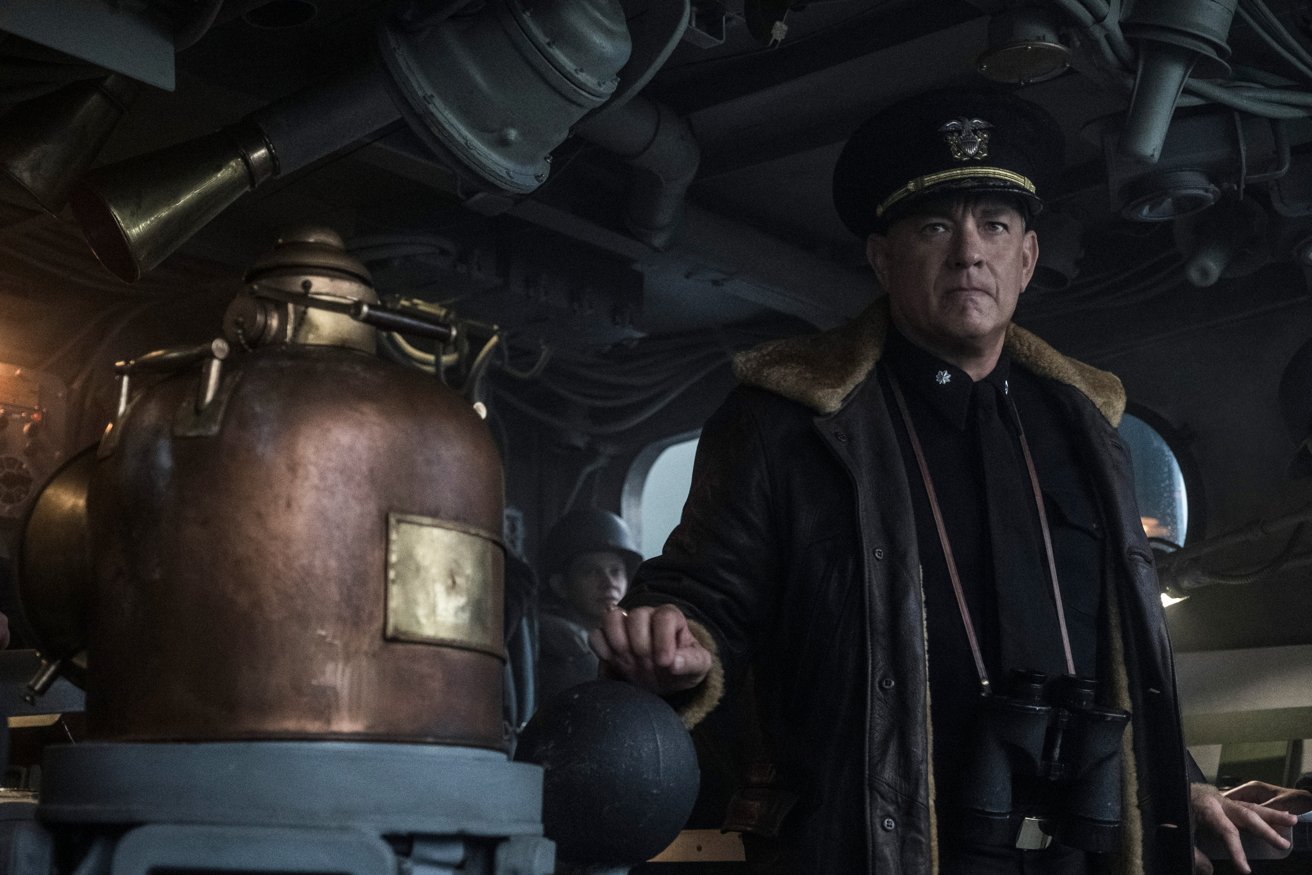 A navy officer stands in a submarine's control room, holding a globe. A brass device is prominently displayed in the foreground.