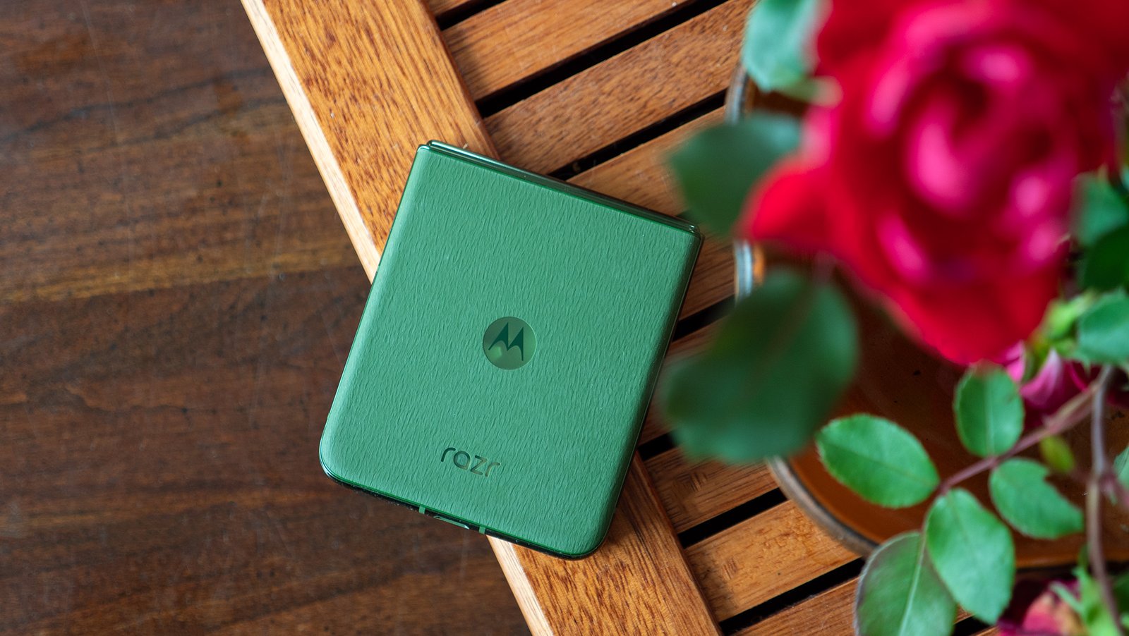 The back of the green Motorola Razr Plus 2024 while it's closed, sitting on a tea tray next to some roses
