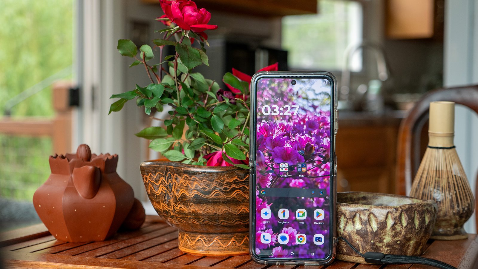 The Motorola Razr Plus 2024 open with its home screen showing, on a tea tray next to some roses and tea pots