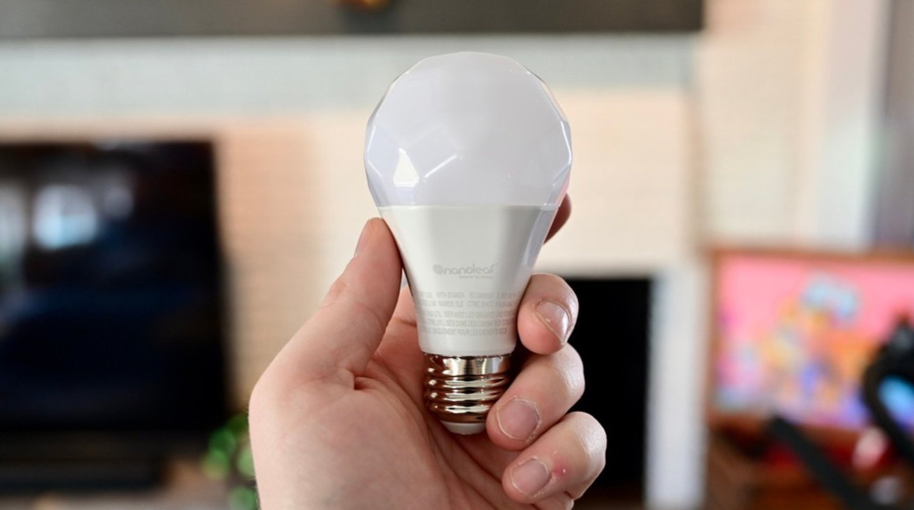 A person holding a white LED light bulb against a blurred indoor backdrop.