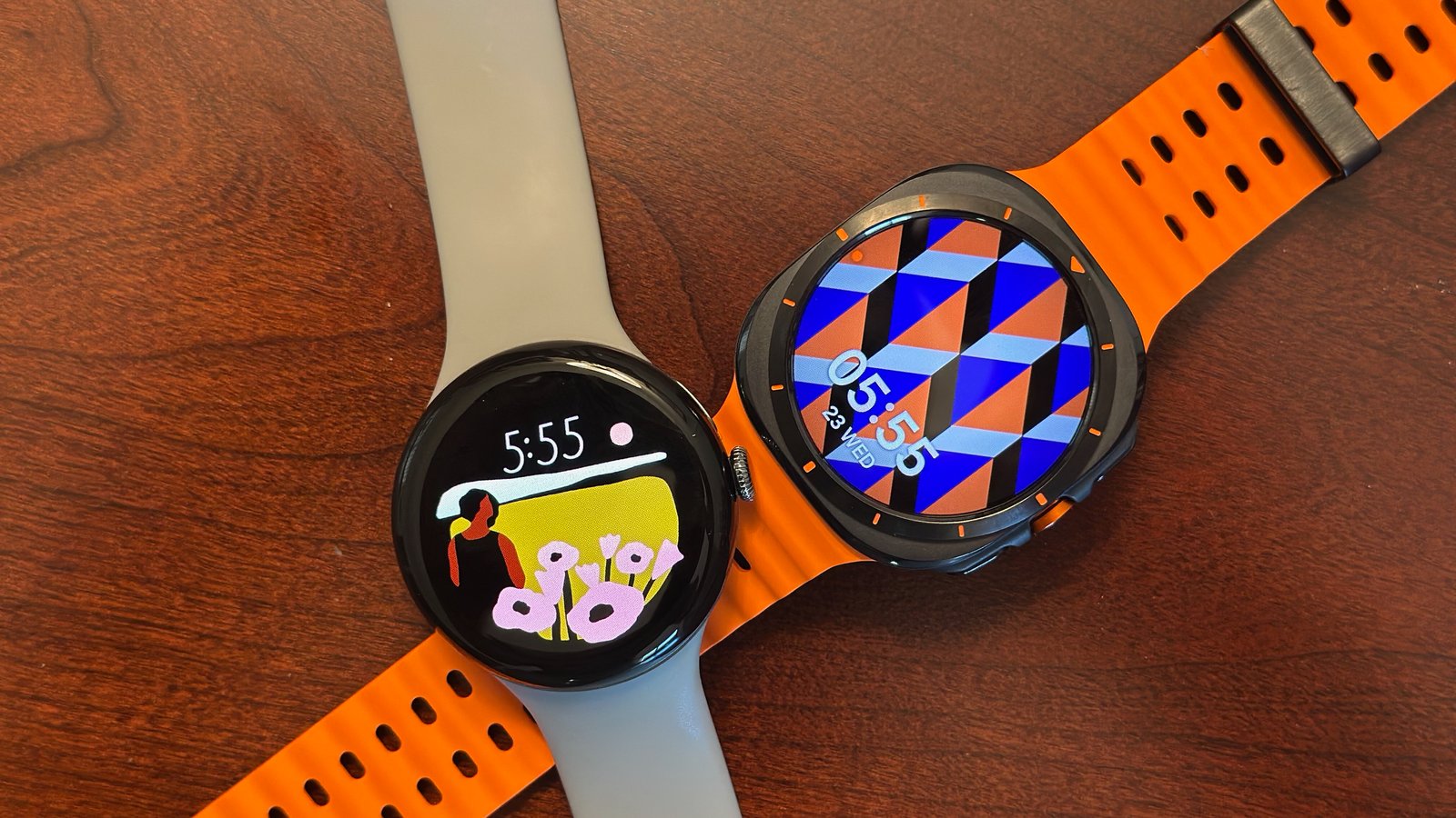 The Google Pixel Watch 3 next to the Samsung Galaxy Watch Ultra on a wooden table, both showcasing vibrant watch faces.