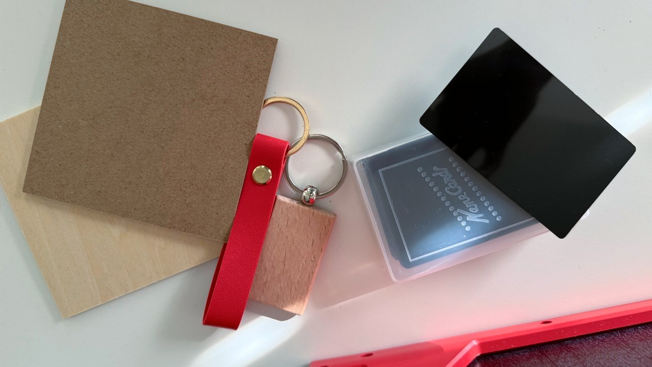 Assorted objects on a light surface: wooden squares, red-strap keychains, clear card case with black card, and a partially visible red object.