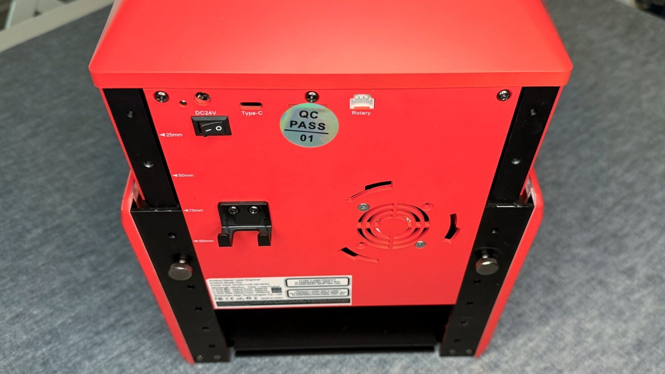 Red device with black mounts, labeled buttons and ports, a circular fan vent, and a QC PASSED sticker on a gray surface.